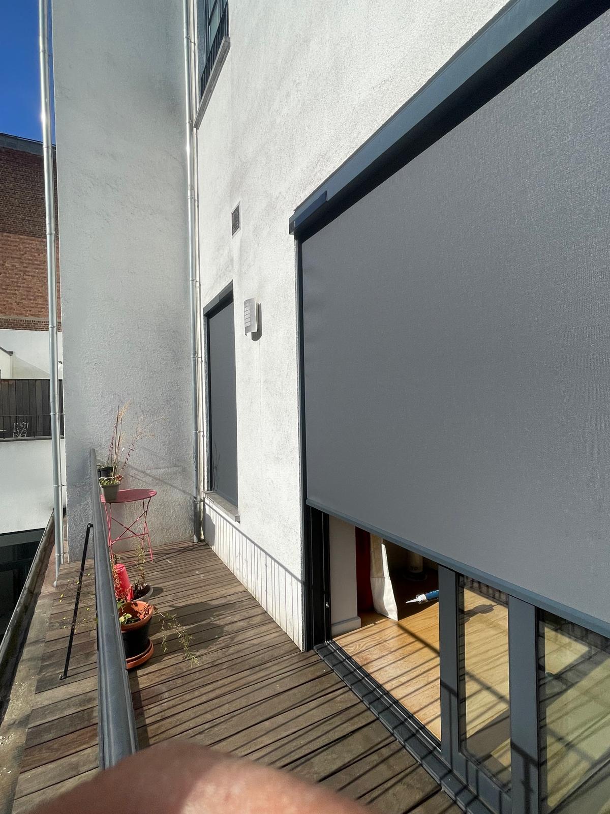 Screen solaire posé par Blindsup devant une baie vitrée donnant sur une terrasse en ville